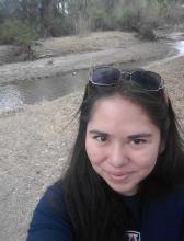 Angelica Serrano headshot, female, wearing a dark shirt, long dark hair, desert setting, water creek